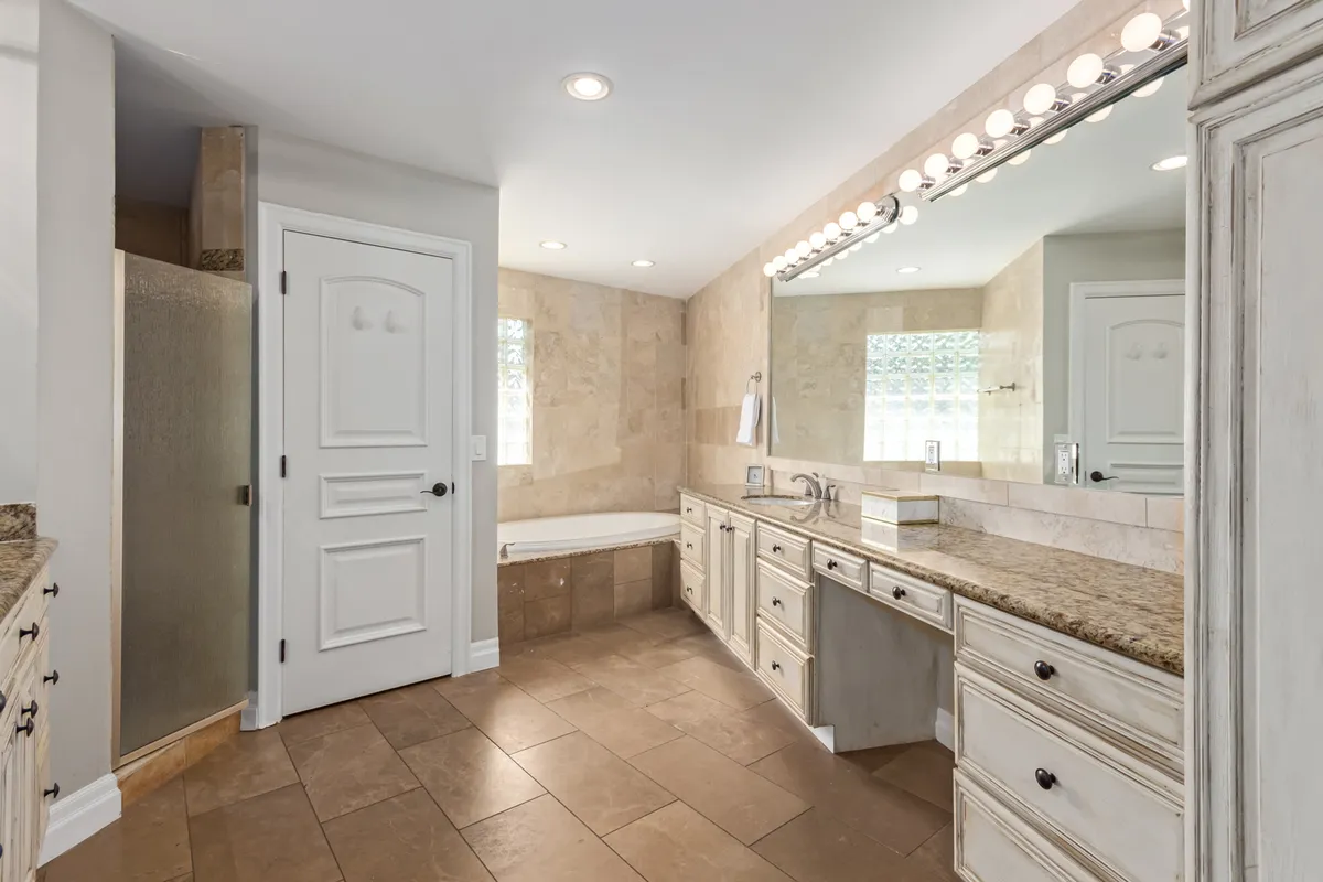 A luxurious en-suite bathroom with a soaking bathtub, double sink vanity with a large mirror, and separate shower area. The space exudes a spa-like ambiance of relaxation and indulgence.