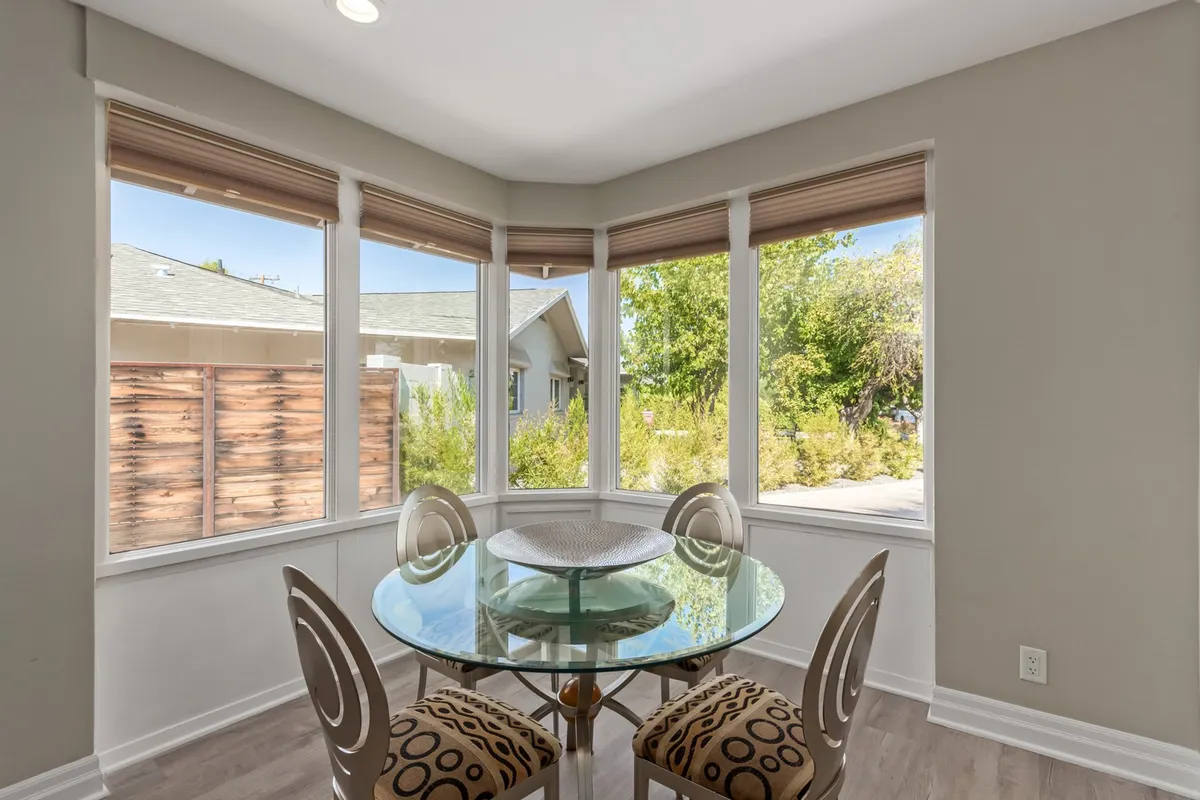 A modern dining area with a glass dining table, decorative bowl centerpiece, stylish chairs, and expansive windows that flood the room with natural light. The layout creates a welcoming spot for casual meals, group gatherings, or morning coffee with a view.