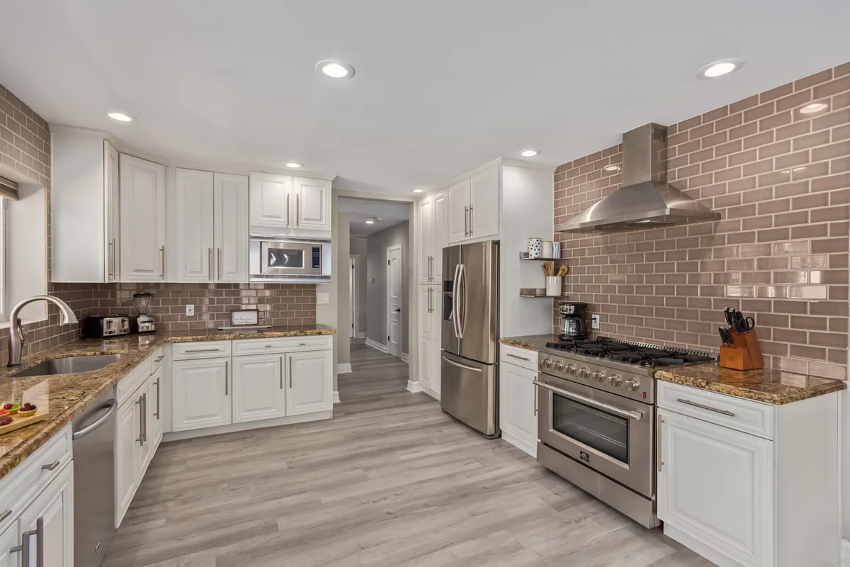 This interior image features a stainless steel gas range, expansive granite countertops, and a tiled backsplash, all within a kitchen setting. The layout allows for clear views of the workspaces, appliances, and an inviting prep area, giving a sense of both functionality and style.