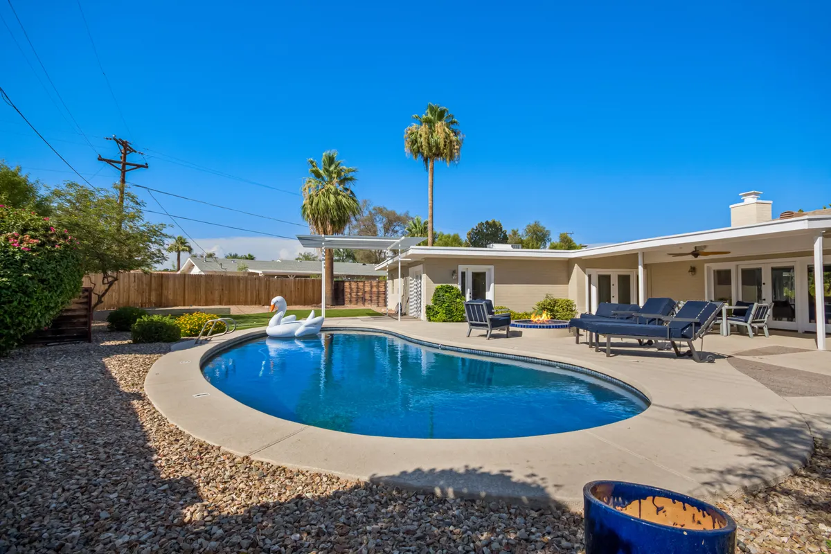 A beautiful backyard oasis featuring a sparkling swimming pool with lounge chairs and palm trees. A decorative swan float adds a playful touch, while the area invites relaxation and group gatherings under the sun.