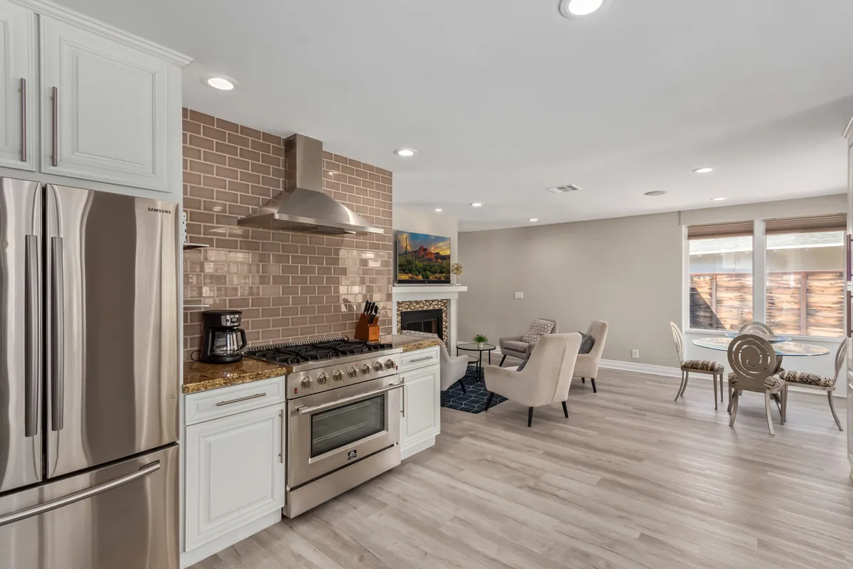 This warm, welcoming kitchen scene showcases a blend of stainless steel appliances, granite countertops, an exposed brick backsplash, and a cozy fireplace. The design balances functionality and ambiance, ideal for both everyday meals and special occasions.