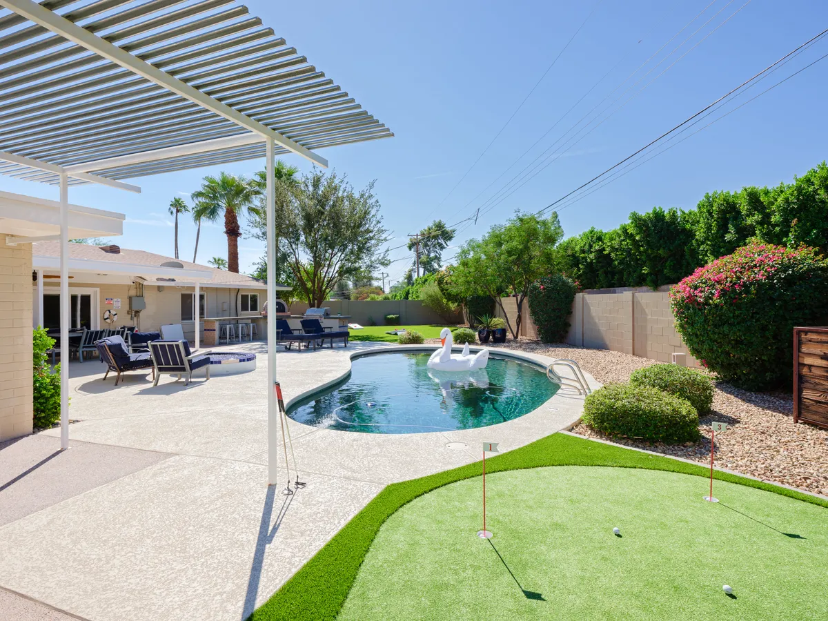 A private backyard oasis featuring a sparkling swimming pool, a lush putting green, comfortable seating under a pergola, and palm-fringed landscaping. The setting invites both relaxation and active play, encapsulating the transition from outdoor adventure to serene leisure described in the content.